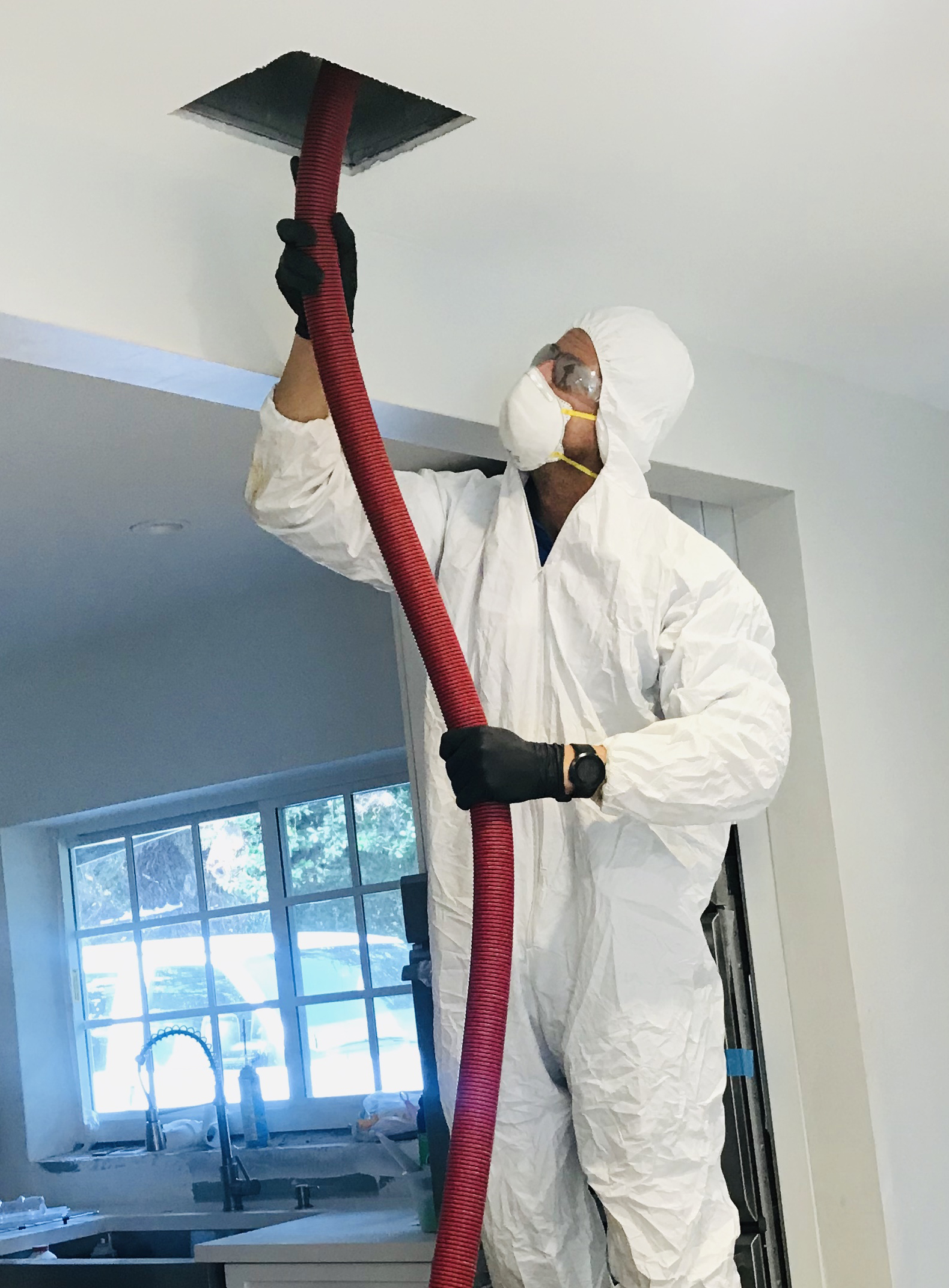 a man in white suit with face covered with mask is cleaning duct